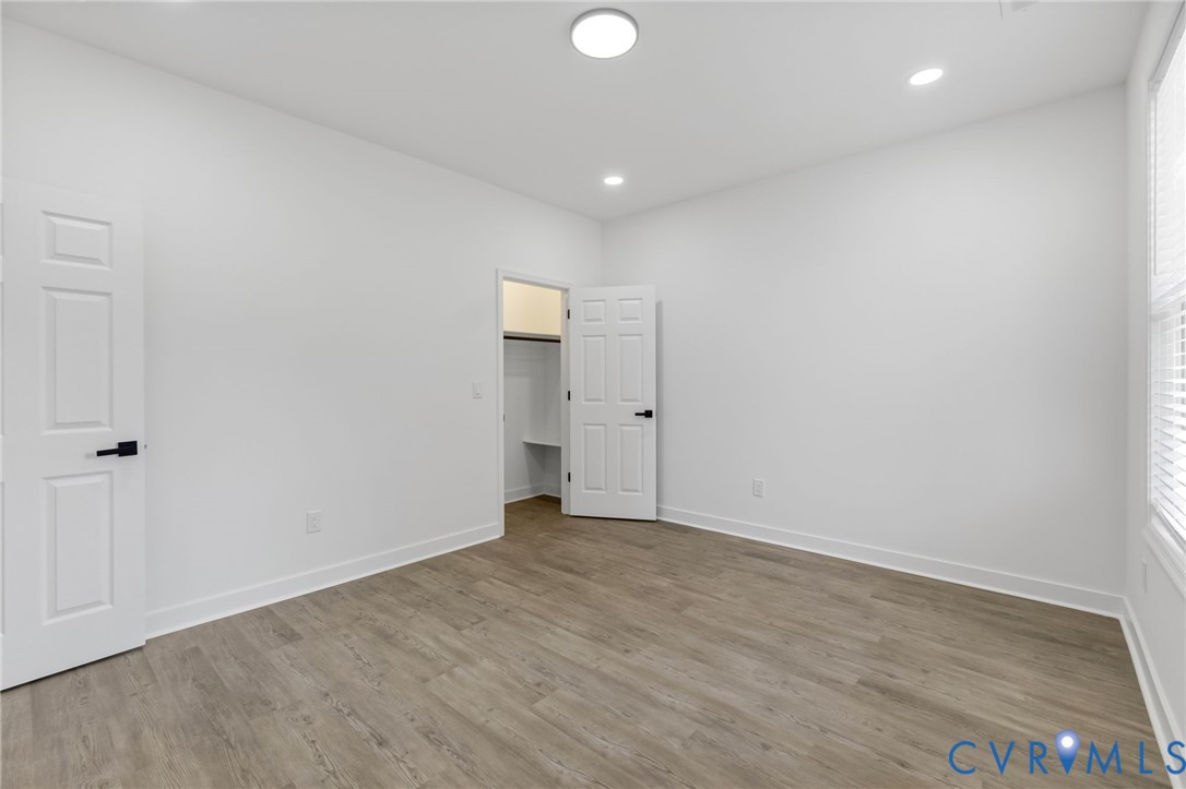 Room featuring wood-finish flooring, white walls, and a window with blinds