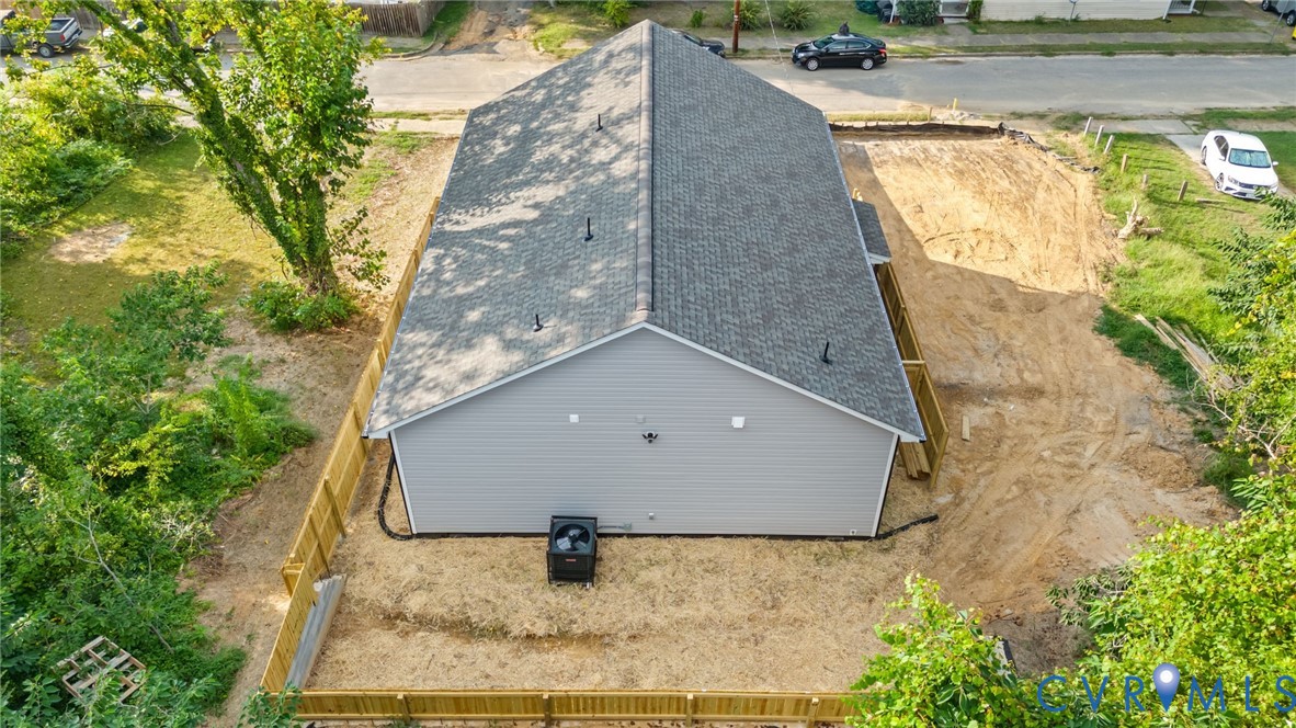 Newly constructed residence featuring a gray exterior, dark shingle roof, and a wood privacy fence