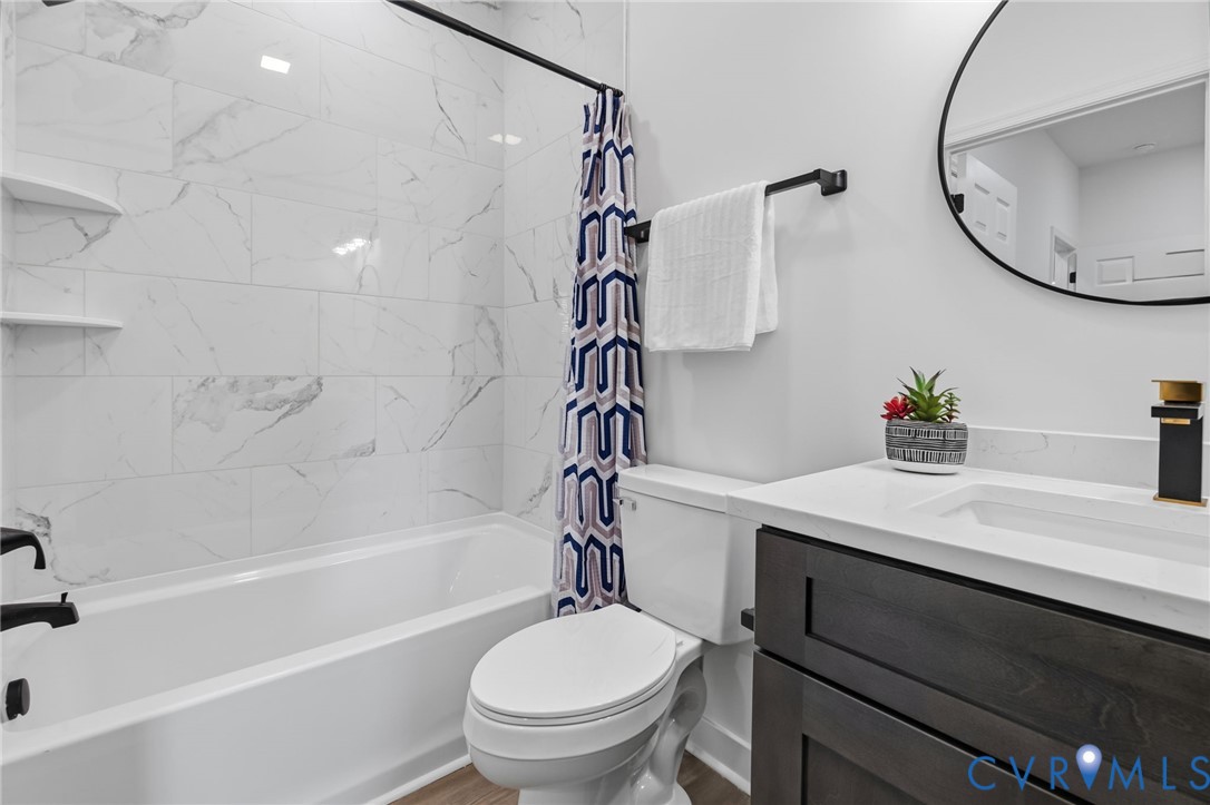 White subway tile with subtle grey veining, built-in tub with matte black fixtures, dark wood-finish vanity with a white countertop, rectangular undermount sink, and a circular black-framed mirror