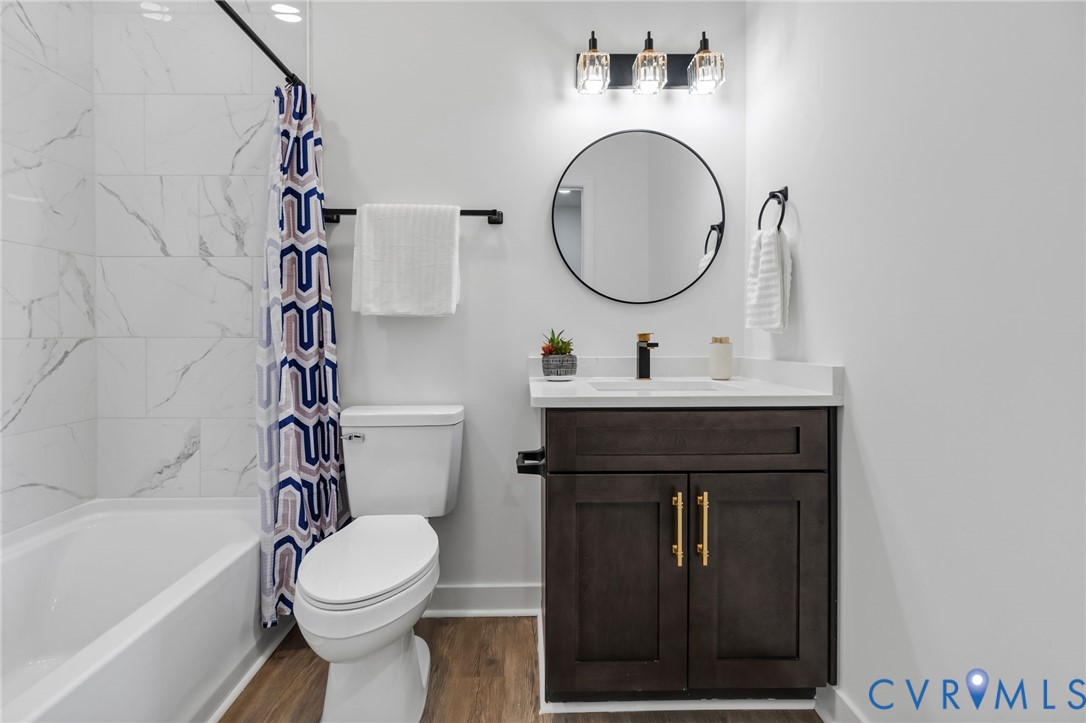 Bathroom featuring a dark wood-finish vanity with gold-tone hardware, a circular mirror, and a three-light vanity fixture