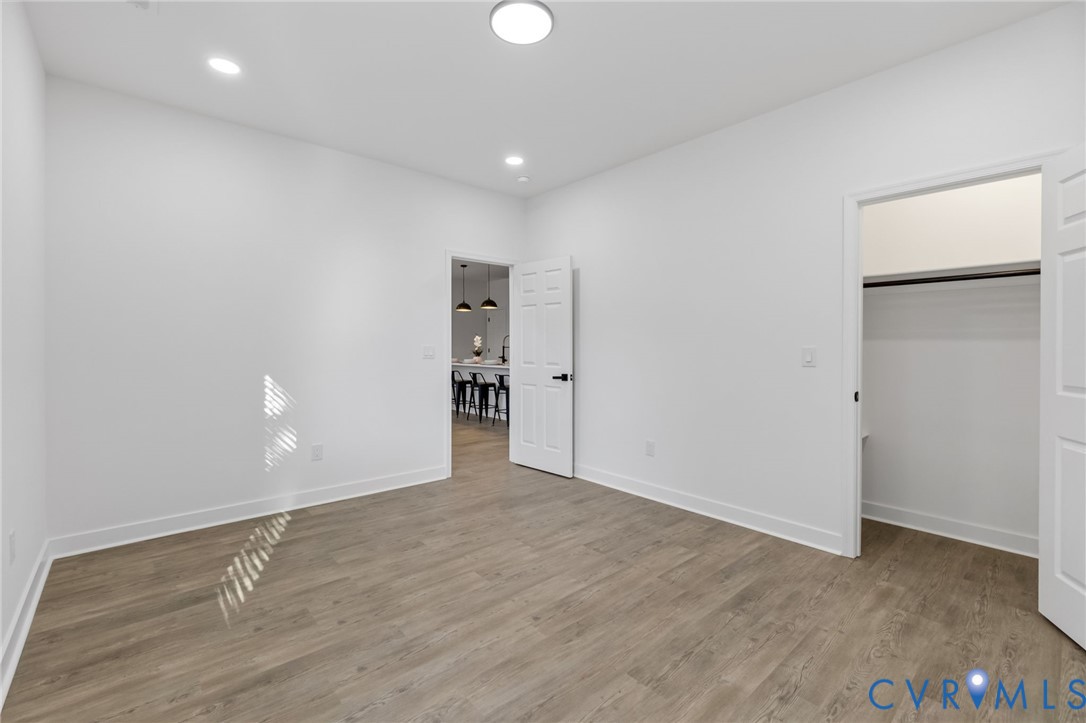 Recessed lighting, wood-finish flooring, white walls, and a built-in closet with a hanging rod