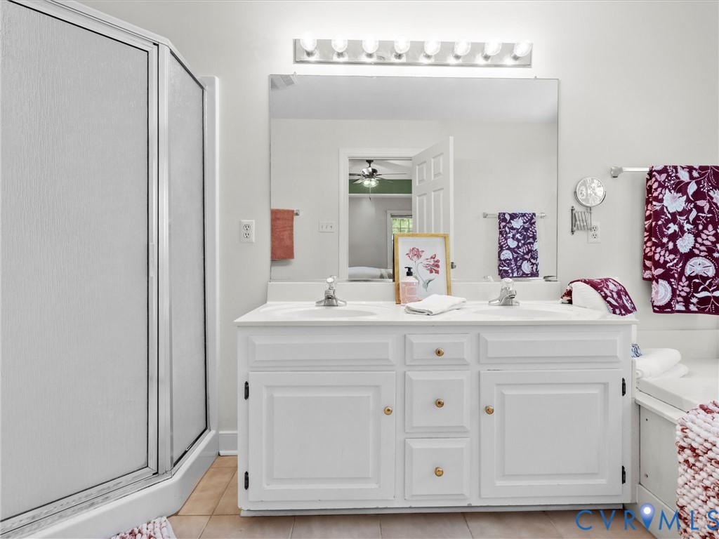 Dual vanity with white cabinetry and integrated sinks, a large mirror, overhead vanity lighting, and a walk-in shower with frosted glass enclosure