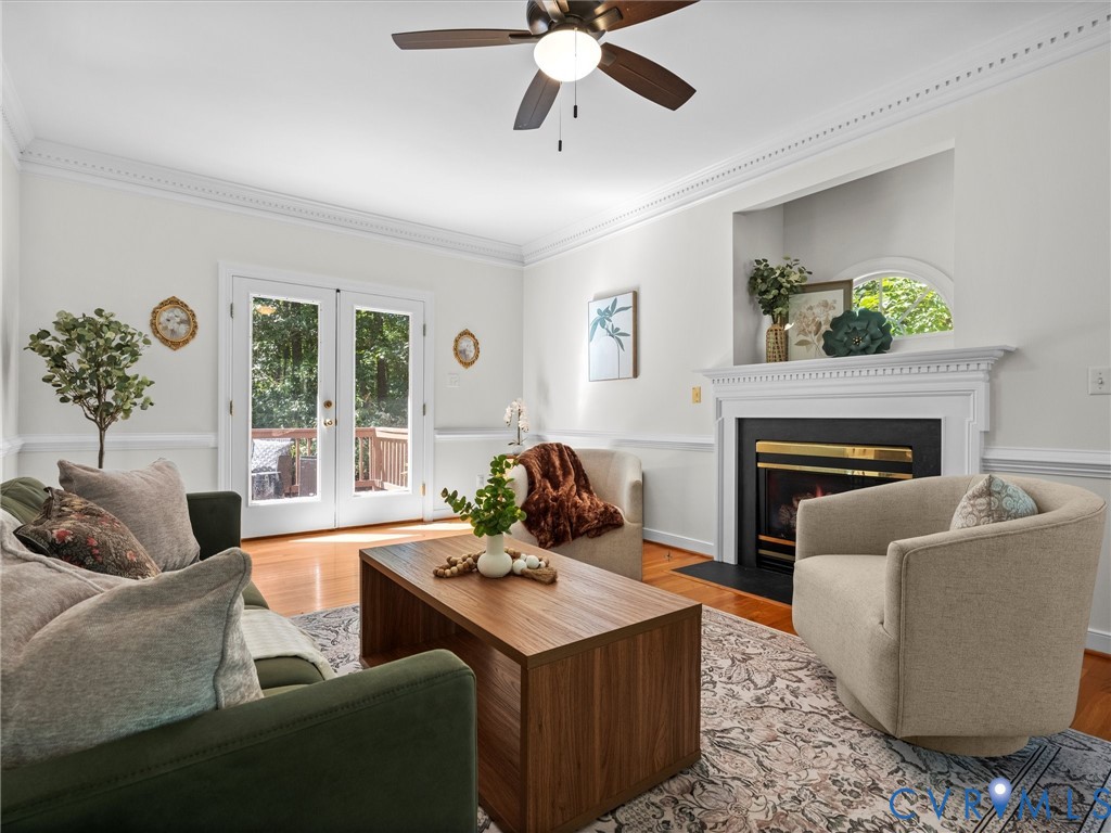 Recessed fireplace with white mantel, French patio doors, wood-finish flooring, ceiling fan, and decorative crown molding