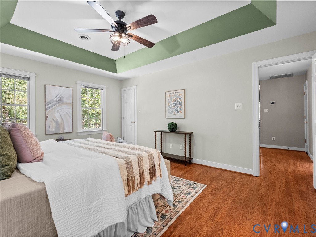 Tray ceiling with recessed lighting, wood-finish flooring, and multiple windows