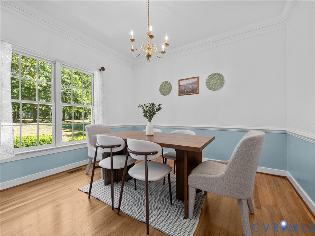 Hardwood flooring throughout, large windows, decorative crown molding, and a chandelier lighting fixture