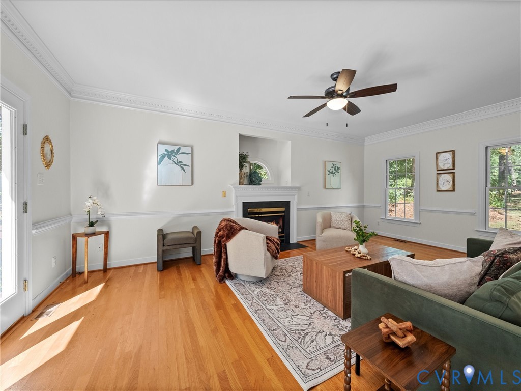 Hardwood flooring, crown molding, fireplace with mantel, ceiling fan, and multiple windows