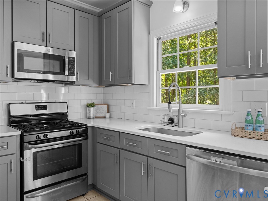 Stainless steel appliances, grey shaker-style cabinetry, white subway tile backsplash, white countertops, and a stainless steel sink