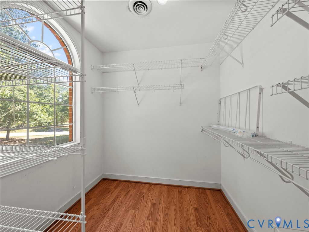 Walk-in closet featuring wire shelving, wood-finish flooring, and an arched window