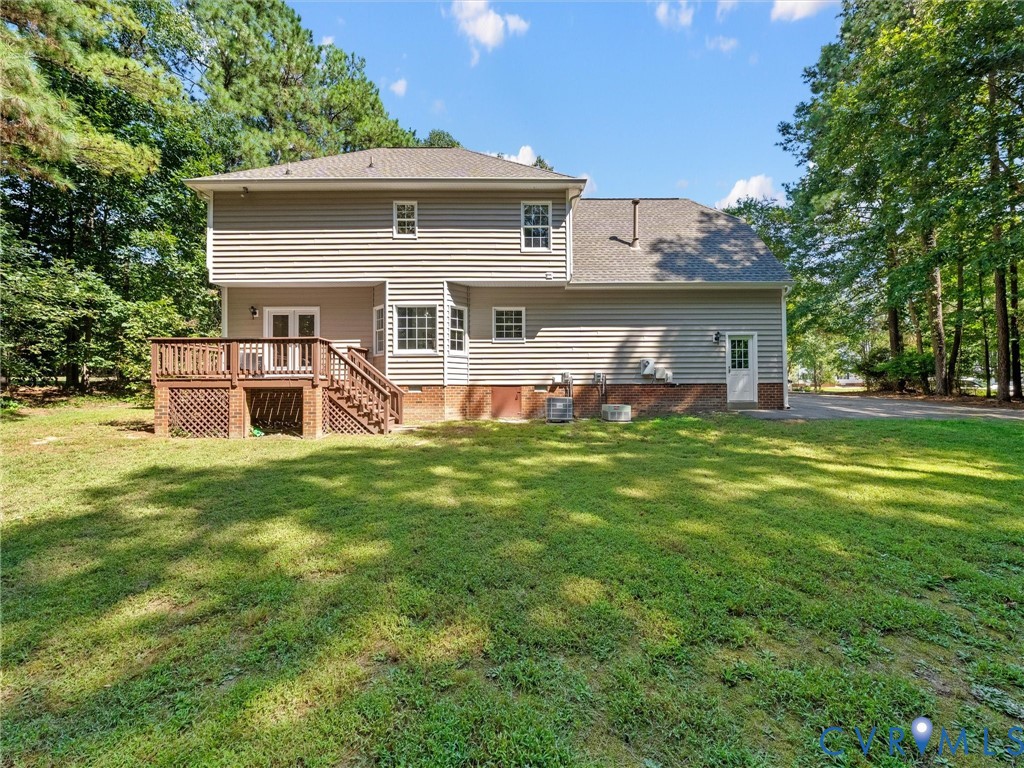 Expansive backyard featuring a wood deck with lattice skirting, double doors, multiple windows, and a paved driveway