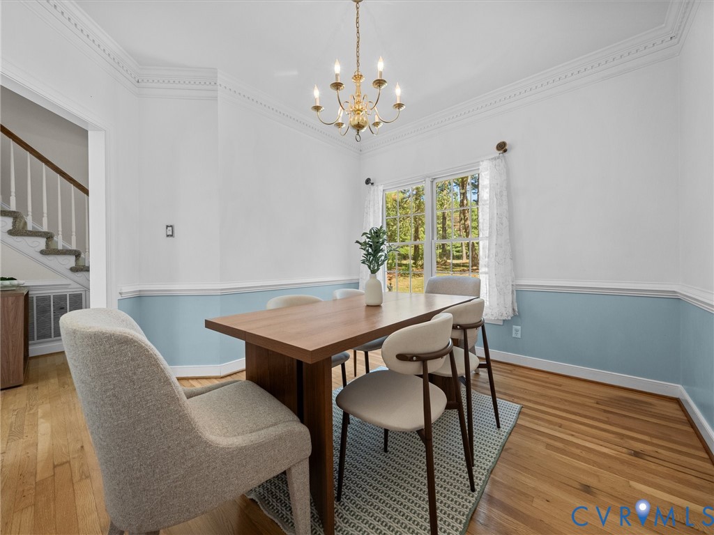 Hardwood flooring, decorative crown molding, and a chandelier illuminate the space