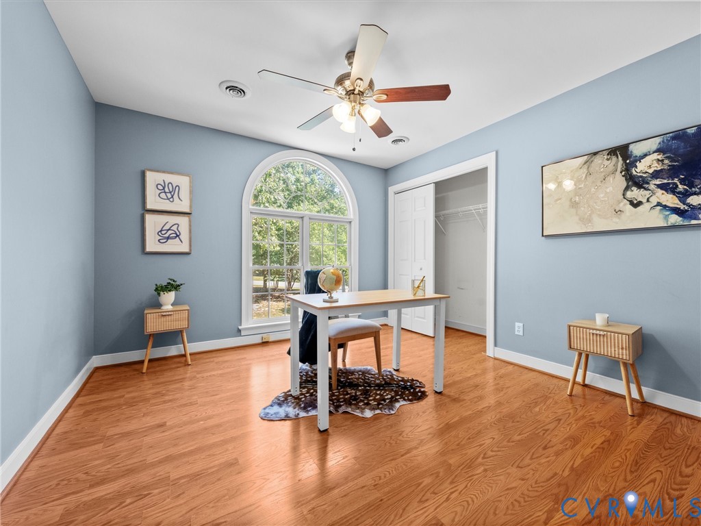 Wood-finish flooring, an arched window, a ceiling fan, a built-in closet with bi-fold doors, and light blue wall paint