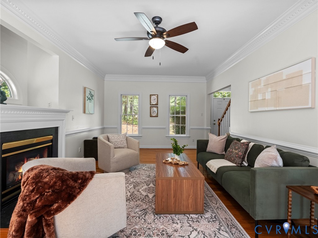 Hardwood flooring, crown molding, chair rail molding, fireplace with a mantel, and a ceiling fan