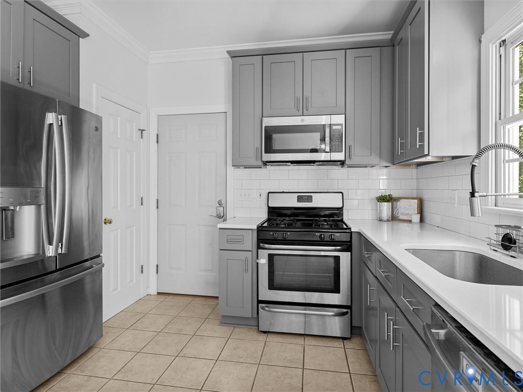 Gray shaker-style cabinetry, white subway tile backsplash, stainless steel appliances, and solid surface countertops