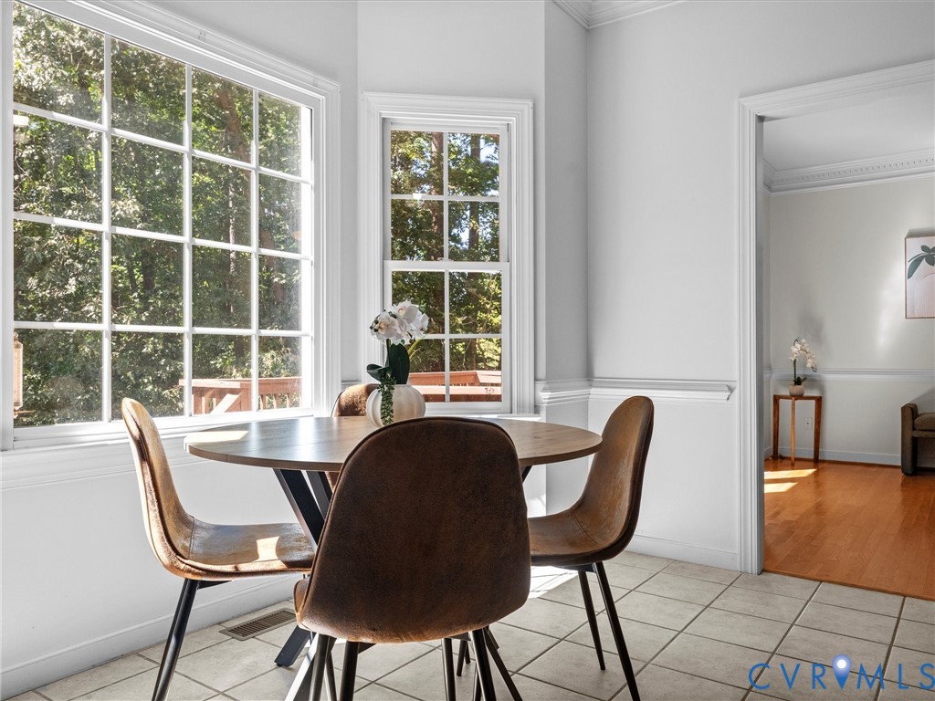 White grid windows, light-toned tile flooring, white crown molding, and a doorway to a room with wood flooring