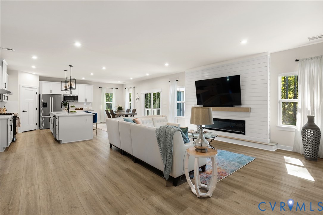 Open-concept living area with wood-finish flooring, recessed lighting, and a shiplap accent wall with a built-in electric fireplace