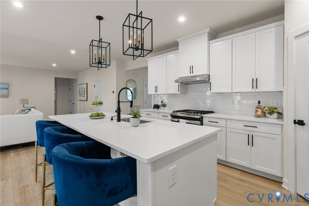 Kitchen featuring a large island with an undermount sink, white cabinetry, integrated stainless steel appliances, and wood-finish flooring