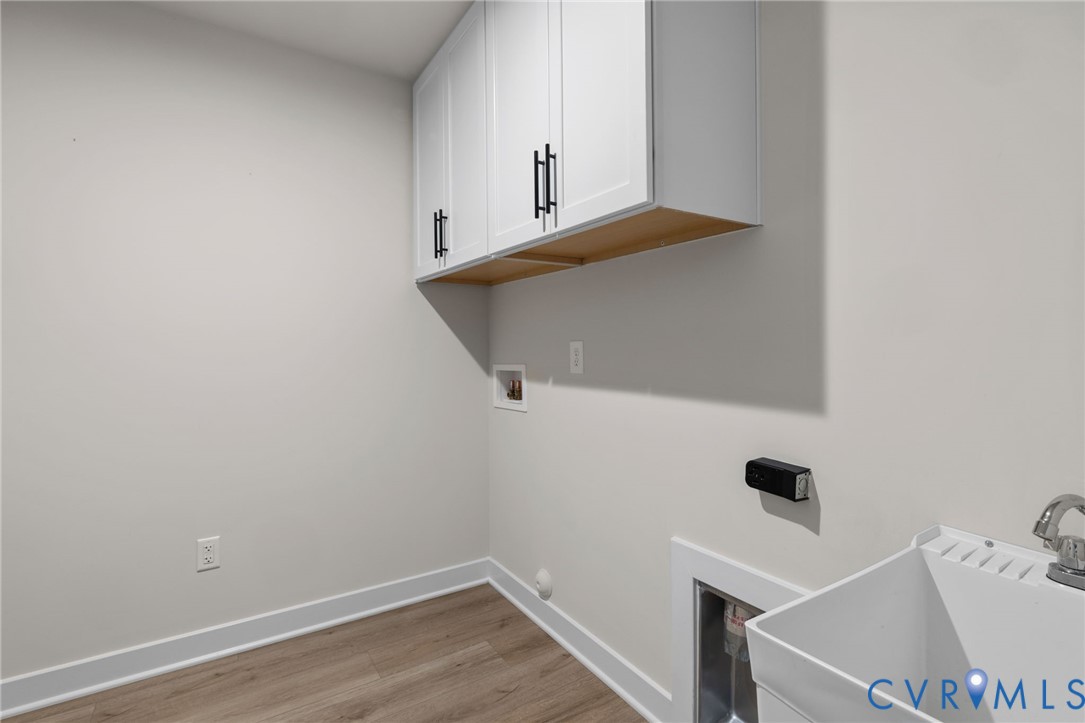 White wall-mounted cabinetry with matte black hardware, utility sink with chrome faucet, and wood-finish flooring