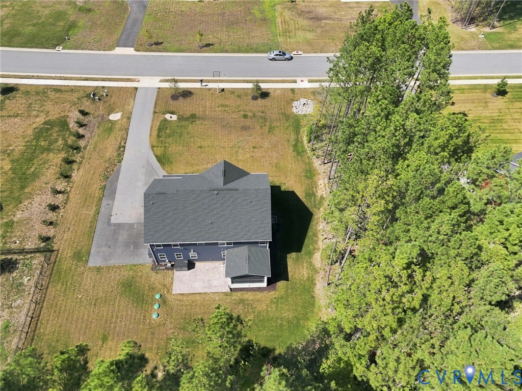 Dark gray roof, light blue siding, paved driveway, stone patio, and surrounding trees