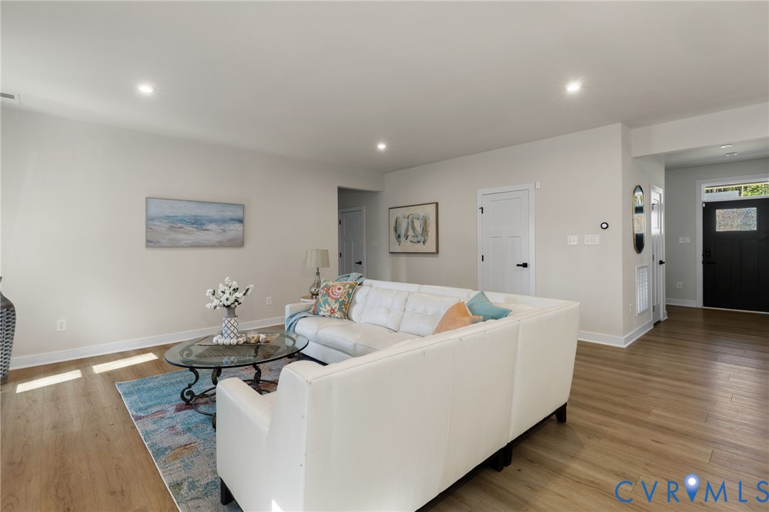 Recessed lighting illuminates the open living space featuring wood-finish flooring and white walls