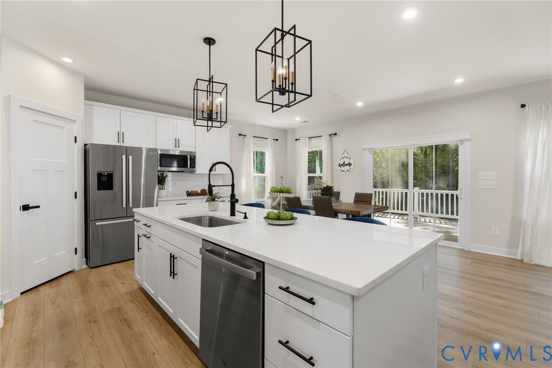 White shaker cabinetry, stainless steel appliances, central island with sink, wood-finish flooring, and sliding glass door