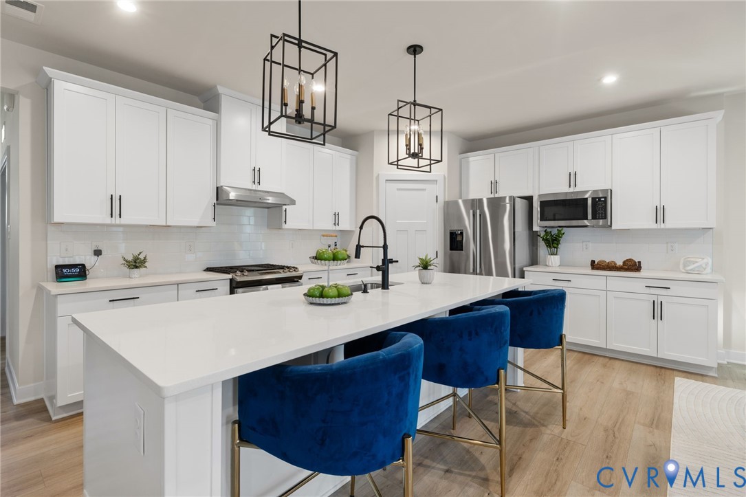 Spacious kitchen featuring white cabinetry, stainless steel appliances, a center island with countertop seating, wood-finish flooring, and pendant lighting