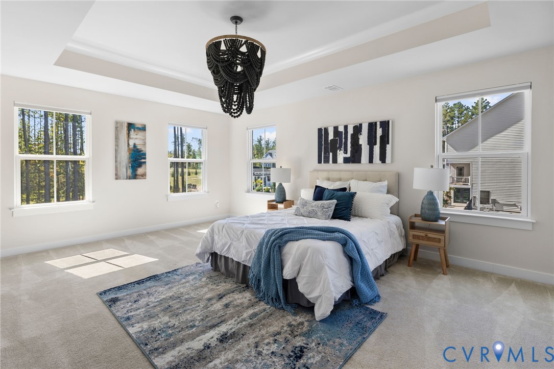 Tray ceiling with a decorative chandelier, light-colored walls, and large windows