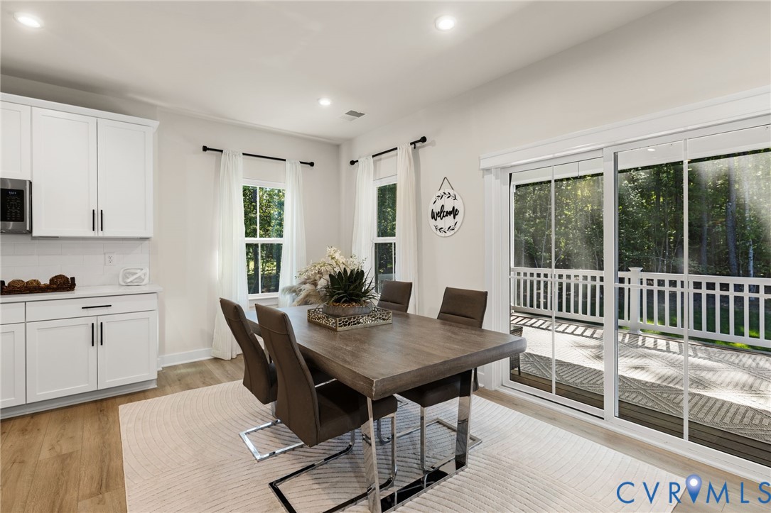 White cabinetry with black hardware, wood-finish flooring, recessed lighting, and a sliding glass door to an outdoor deck