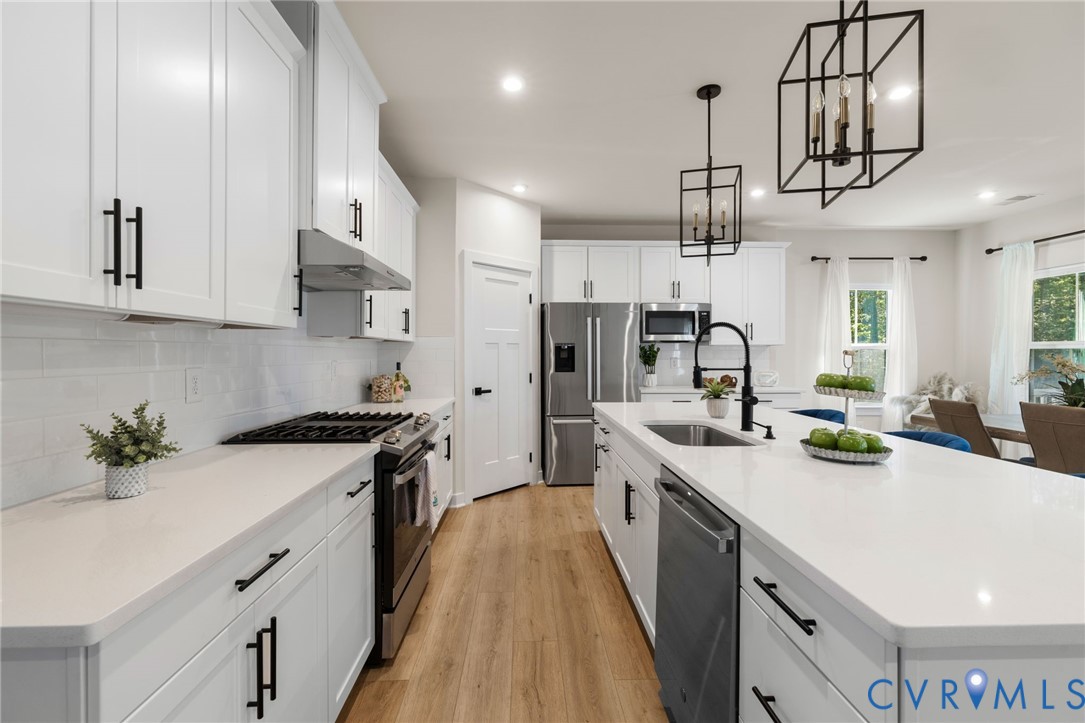 White cabinetry, white countertop surfaces, stainless steel appliances, wood-finish flooring, and black hardware accents