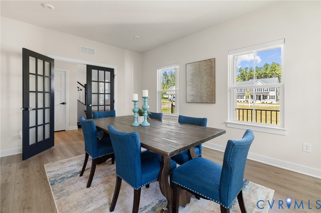 Spacious room featuring light wood-finish flooring, multiple windows, recessed lighting, and black French doors