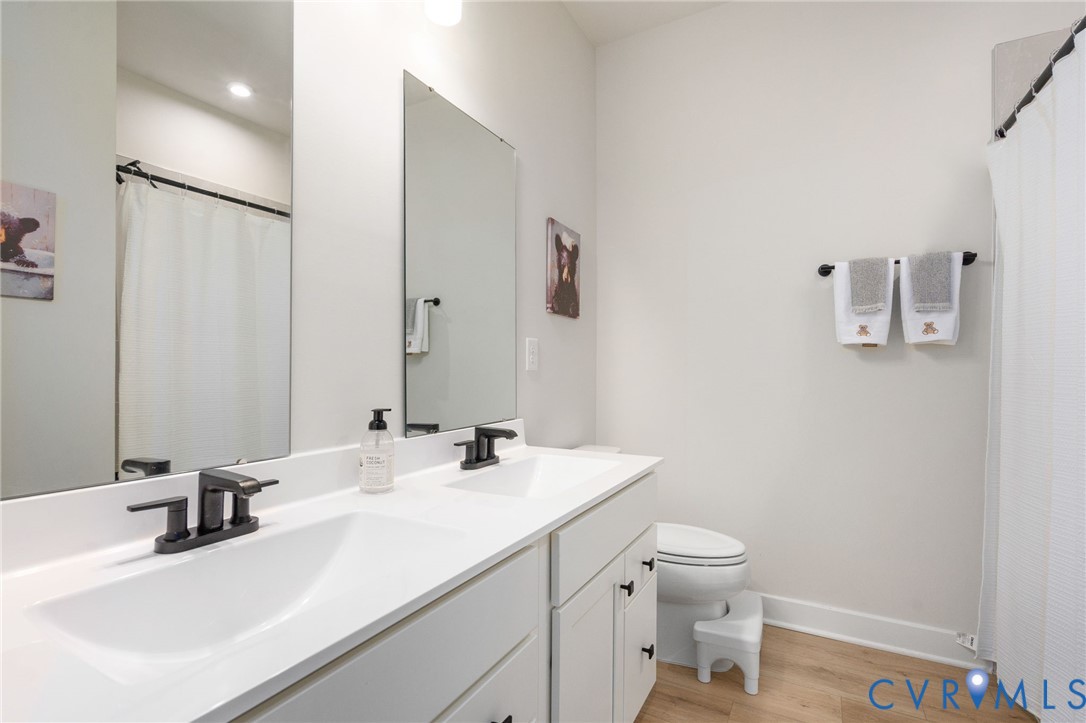 Dual vanity with integrated sinks, matte black fixtures, full-width mirrors, wood-finish flooring, and a white shower curtain