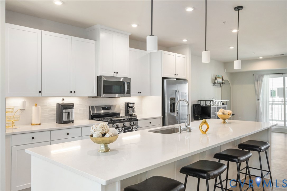 Kitchen featuring white shaker cabinetry, stainless steel appliances, a large center island with an undermount sink, recessed lighting, and pendant lighting