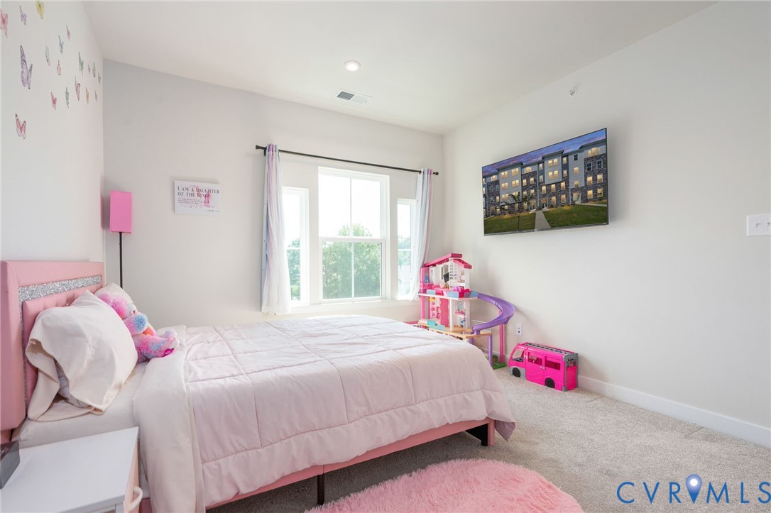 Vaulted ceiling with recessed lighting, wall-mounted television, large window with outdoor greenery, and carpeted flooring