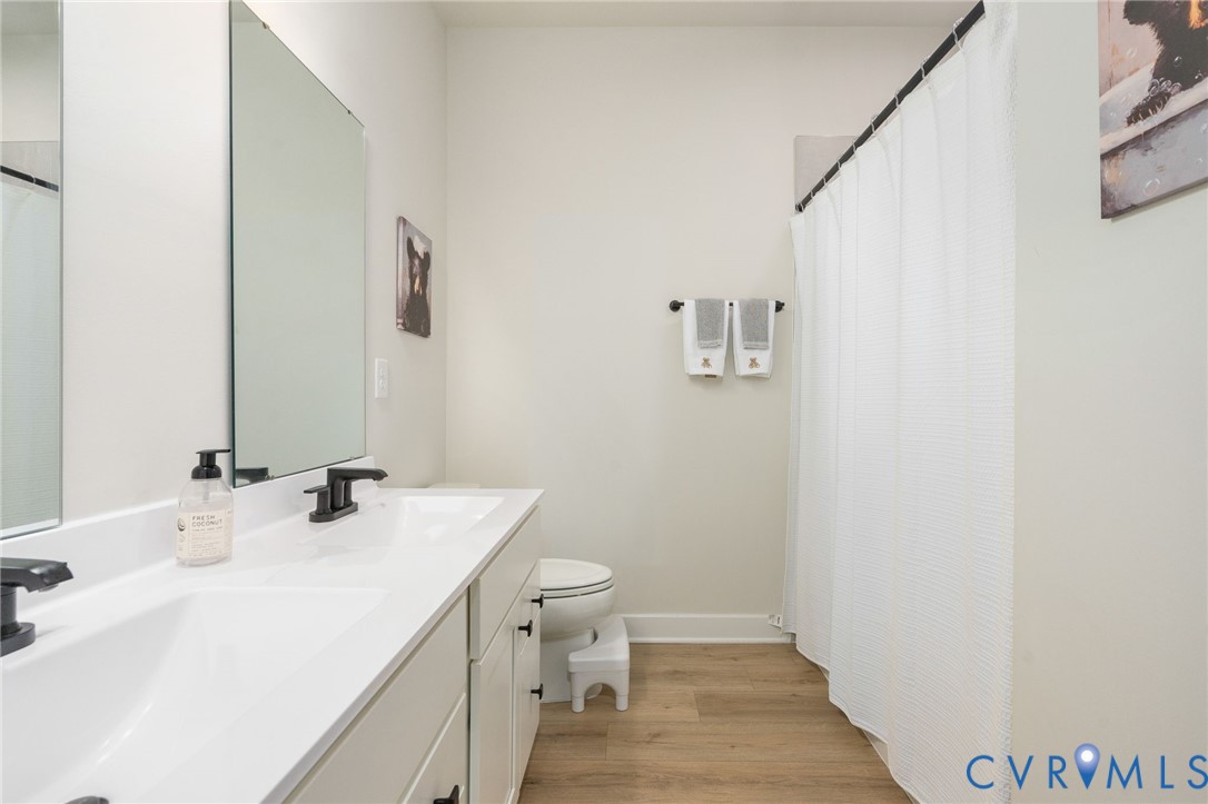 Dual white rectangular sinks, black matte faucets, wood-finish flooring, and a shower with a white curtain