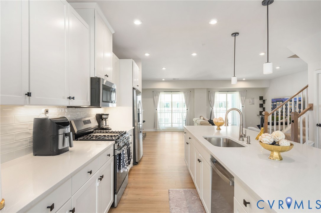 White shaker cabinetry with matte black hardware, stainless steel appliances, a tile backsplash, and stone countertops