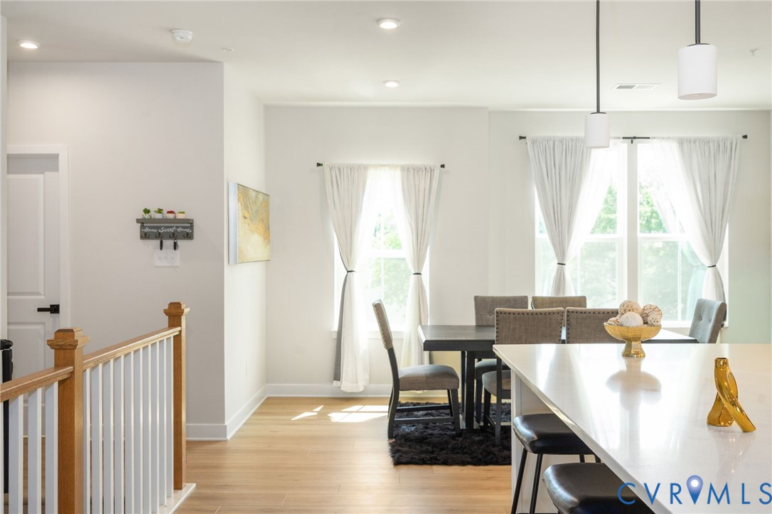 Hardwood-finish flooring, white walls, recessed ceiling lighting, a white kitchen island, and modern pendant lighting