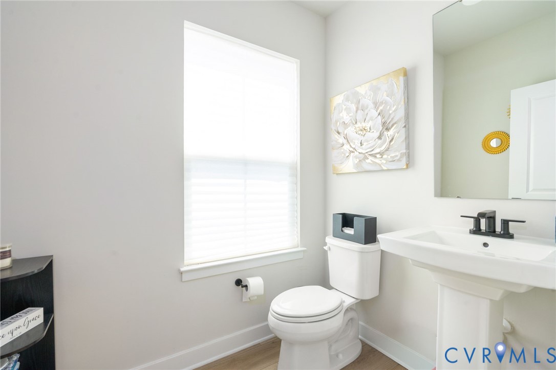 Pedestal sink with black-finish faucet, toilet, and wood-finish flooring