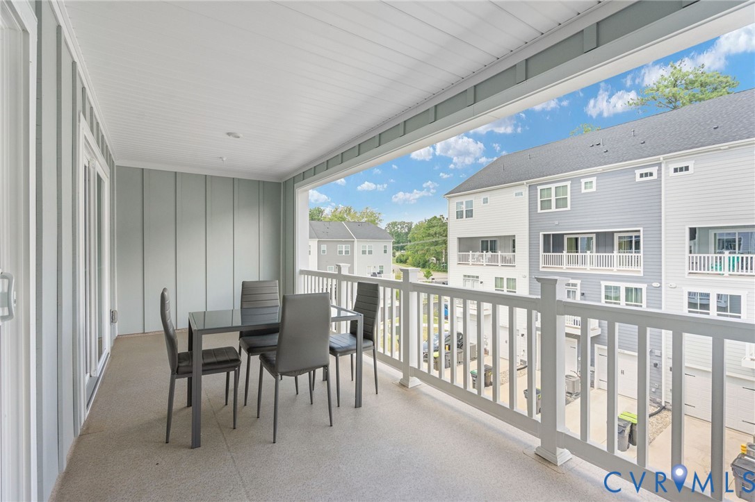 Covered balcony with a durable flooring surface, vertical panel wall siding, and white railing