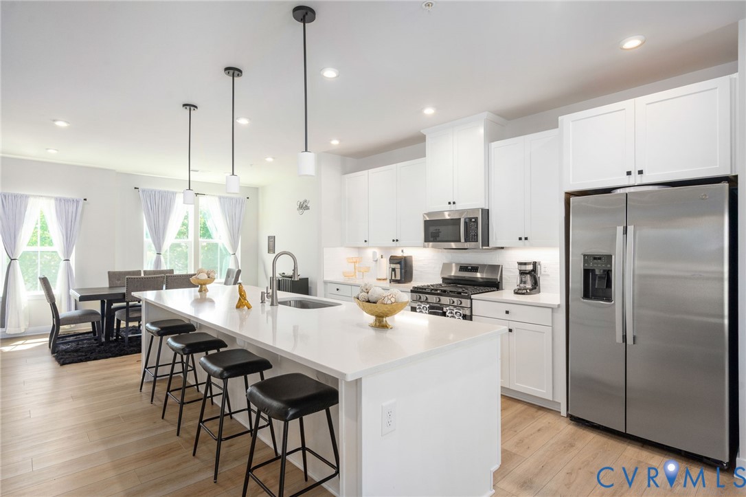 Open-concept kitchen featuring an island with pendant lighting, white cabinetry, stainless steel appliances, and wood-finish flooring