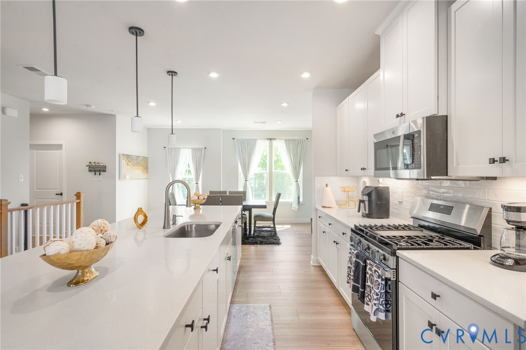 Modern kitchen featuring white cabinetry, stainless steel appliances, a large island with an undermount sink, and wood-finish flooring