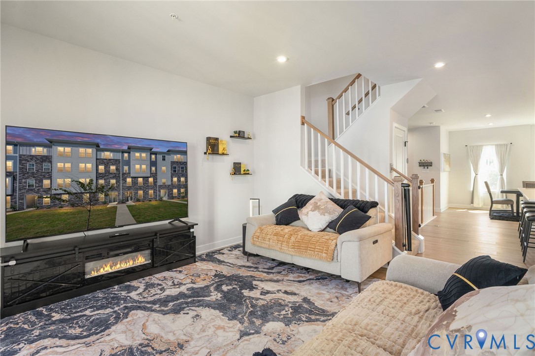 Open-concept living space featuring recessed lighting, a modern electric fireplace, light wood-finish flooring, and a staircase with white balusters and wood handrails
