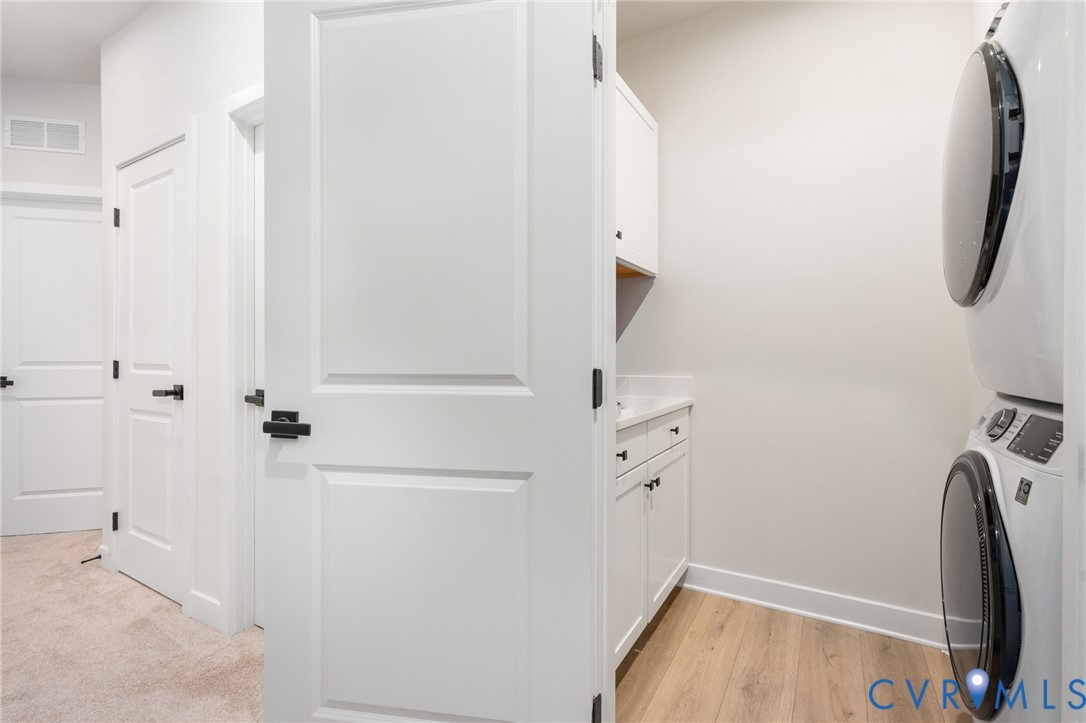 Laundry area with stackable appliances, white cabinetry, a countertop, and wood-finish flooring