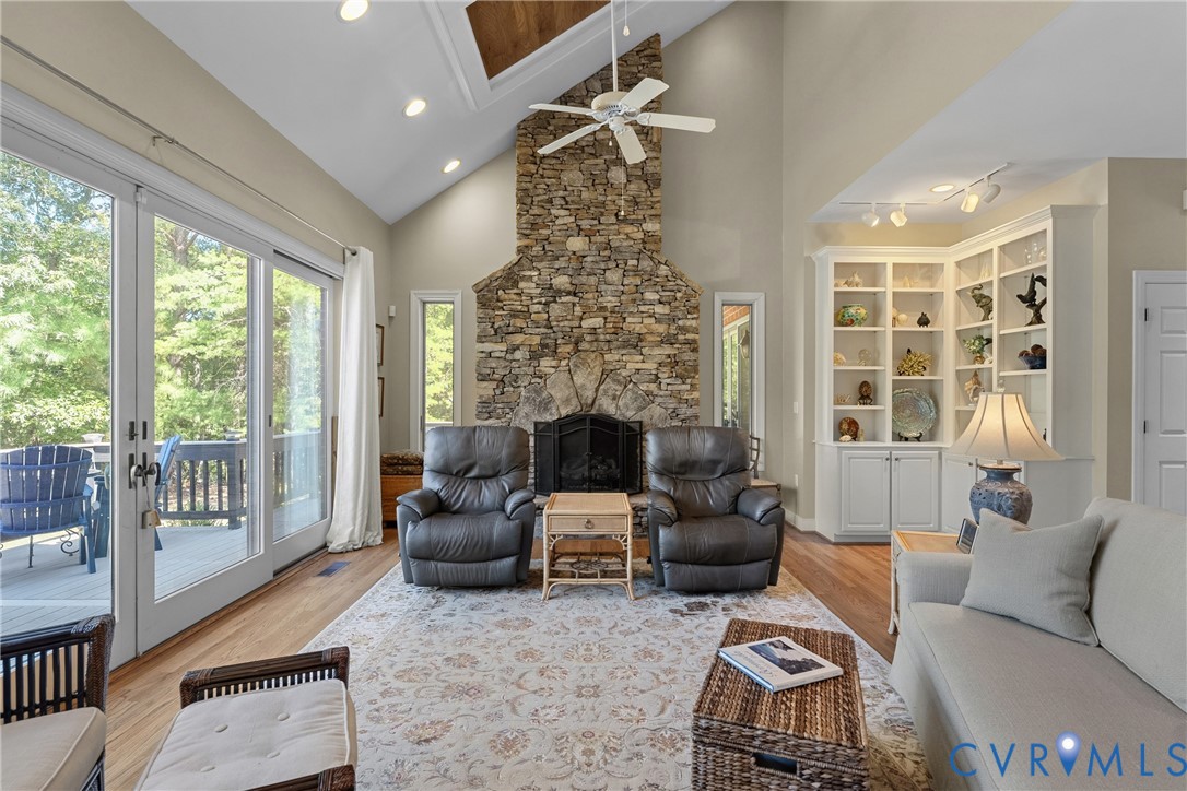 Vaulted ceiling with wood-finish accent, stone fireplace, built-in shelving, wood-finish flooring, and sliding glass doors to outdoor deck