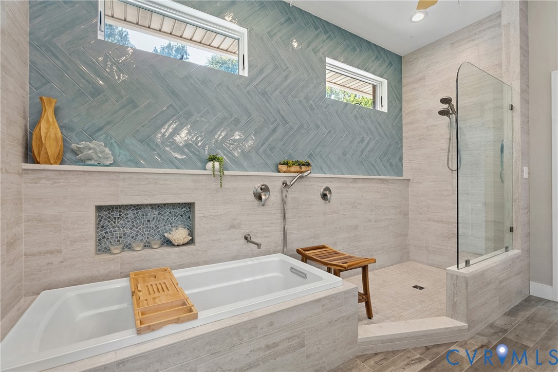 Recessed bathtub with deck-mounted fixtures, walk-in shower with glass enclosure, wall-mounted shower system, and blue herringbone tile accent wall