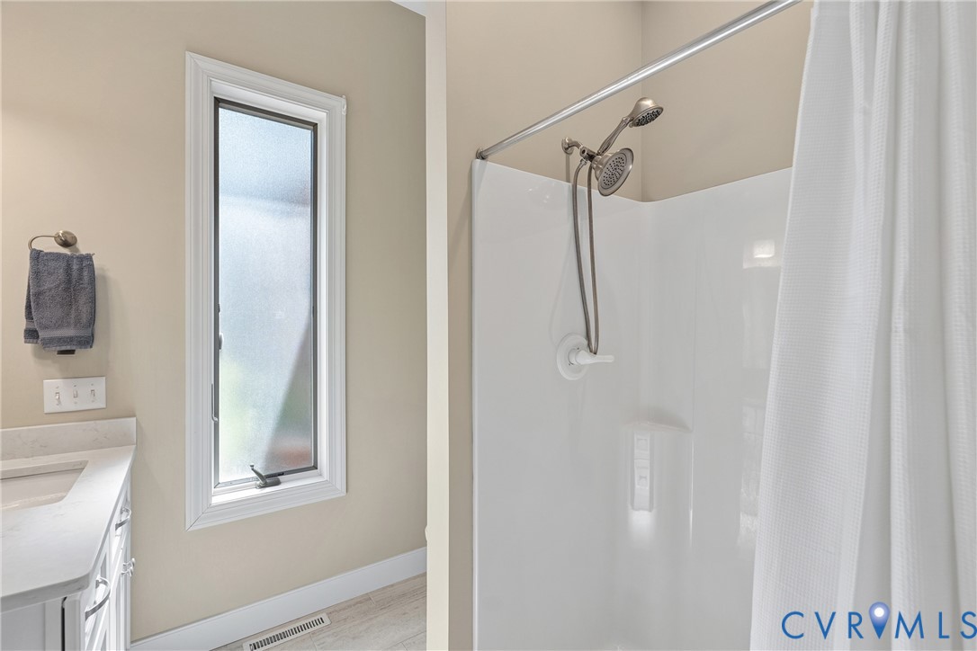 Bathroom featuring a shower with a two-head fixture, a vanity with an undermount sink, and a vertical frosted window