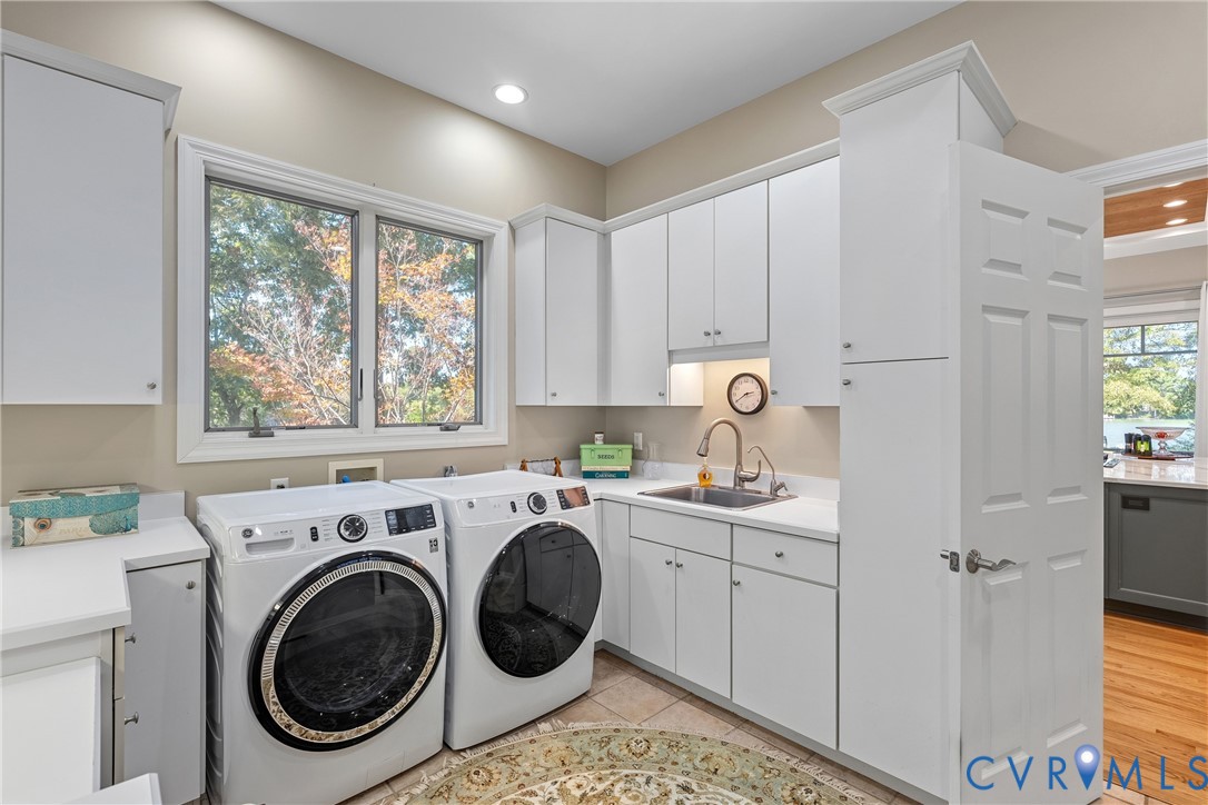 Laundry area with built-in white cabinetry, light-toned countertops, a stainless steel sink with a gooseneck faucet, and a large window