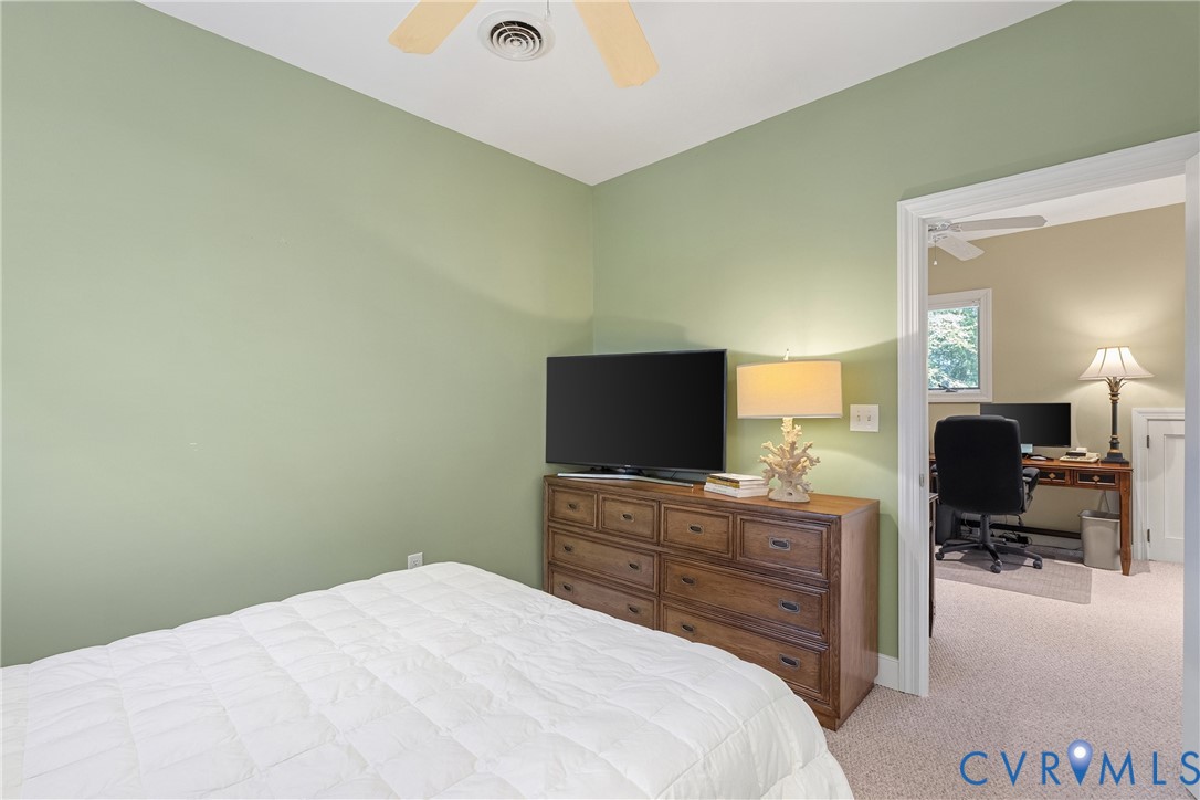 Ceiling fan, light green wall paint, wood-finish dresser, neutral carpet, open doorway