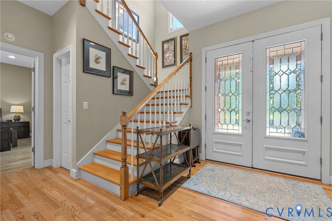 Wood-finish flooring, a wood staircase with white risers, and decorative glass double entry doors