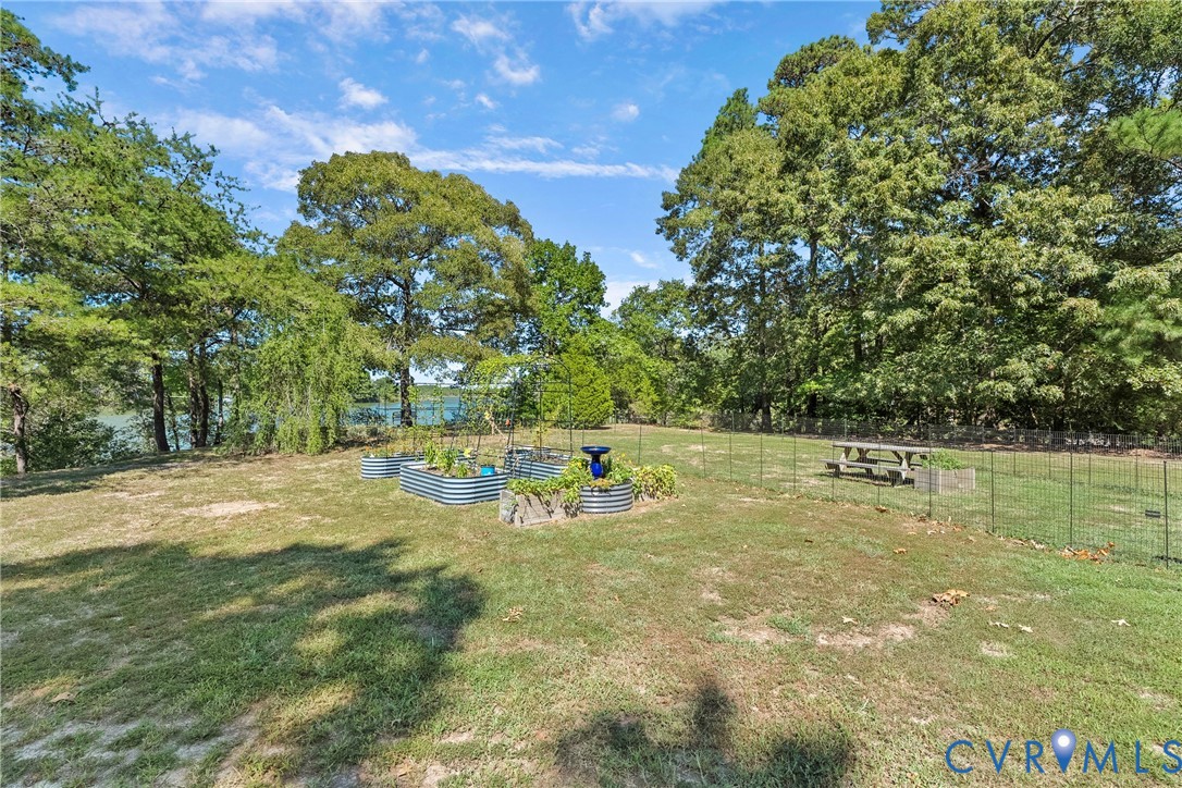 Expansive yard featuring mature trees, raised garden beds, and a metal wire fence enclosure