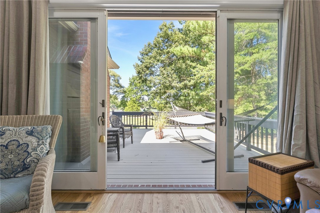 Wood-finish flooring leading to a glass sliding door, opening to an expansive outdoor deck with a black railing system