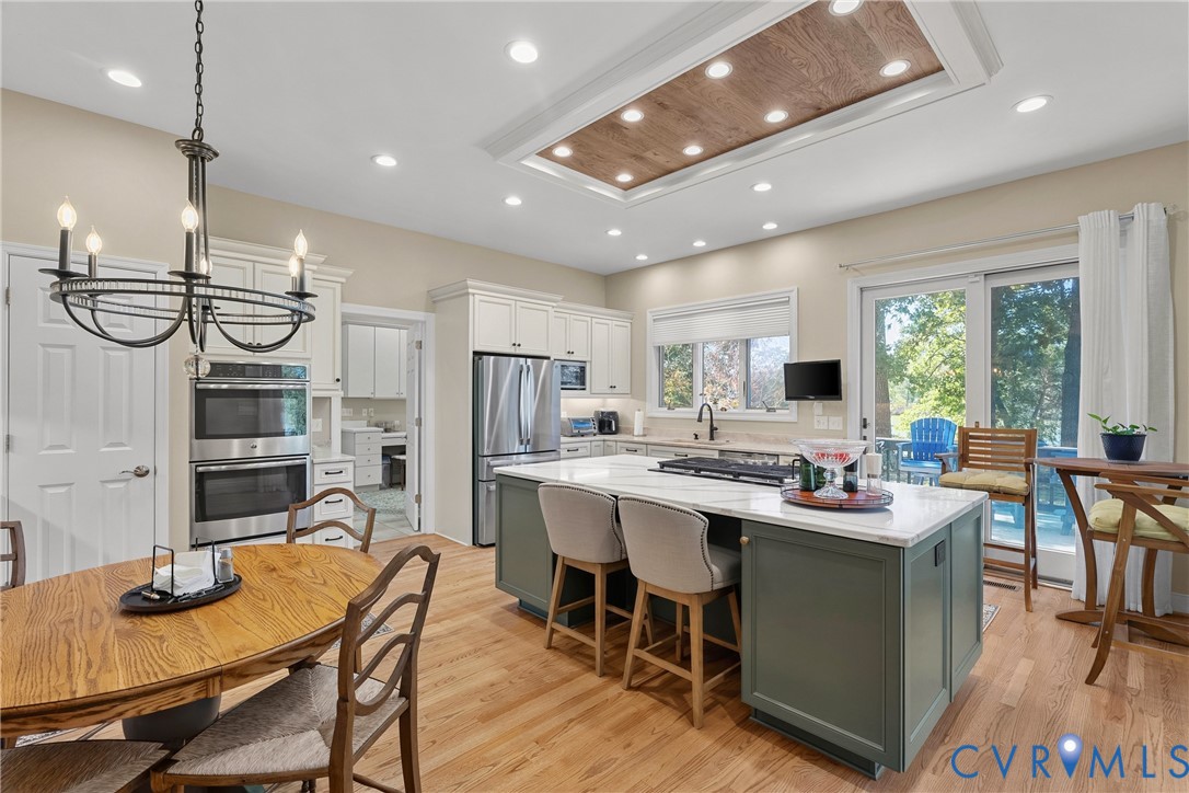 Kitchen featuring light wood-finish flooring, white cabinetry, stainless steel appliances, a center island with countertop seating, and a tray ceiling with recessed lighting